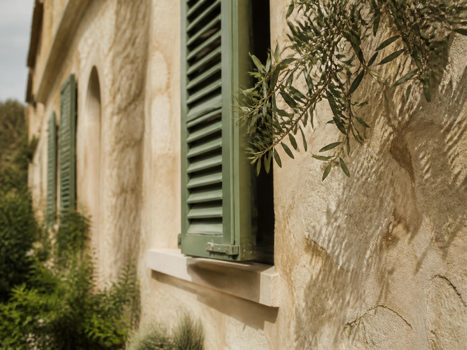 Sandstone facade of a Mallorcan finca with green shutters and an olive branch in morning light